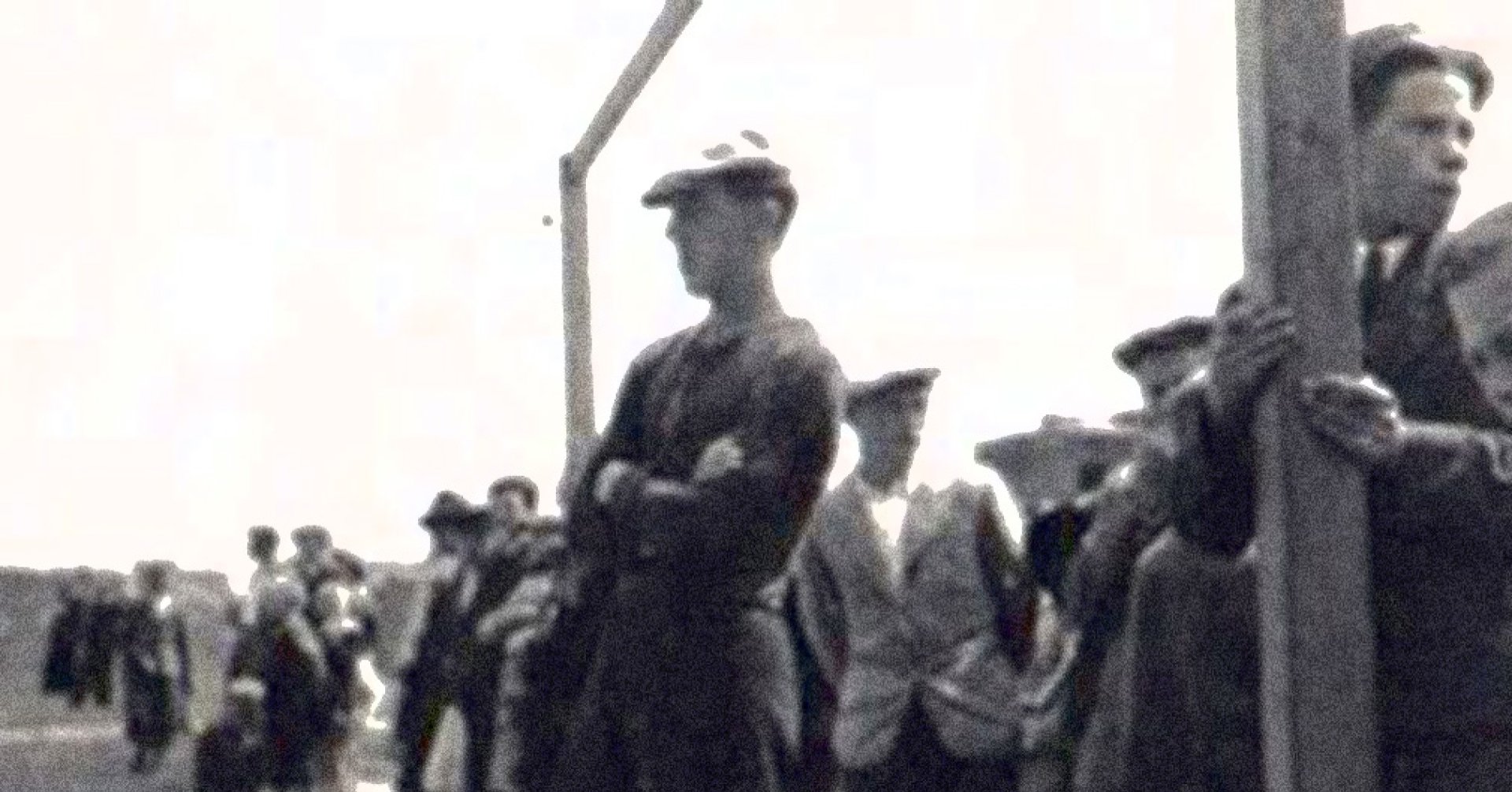 Grupa mężczyzn, na pierwszym planie mężczyzna w kaszkiecie, krótkich spodenkach i getrach