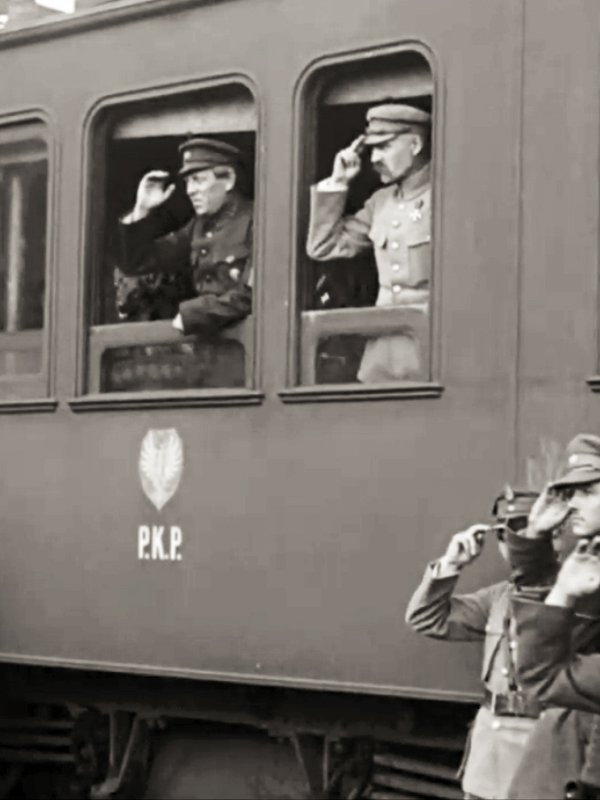 Pociąg PKP, w jednym z okien stoi i salutuje Józef Piłsudski, w drugim Ataman Petlura, przed pociągiem stoją salutujący żołnierze