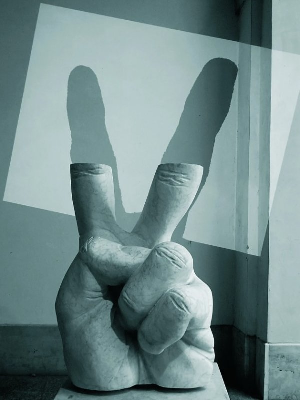 zdjęcie, rzeźba dłoni w geście V, palce wskazujący i środkowy nie posiadają połowy długości, na ścianie rzucony cień brakujących palców