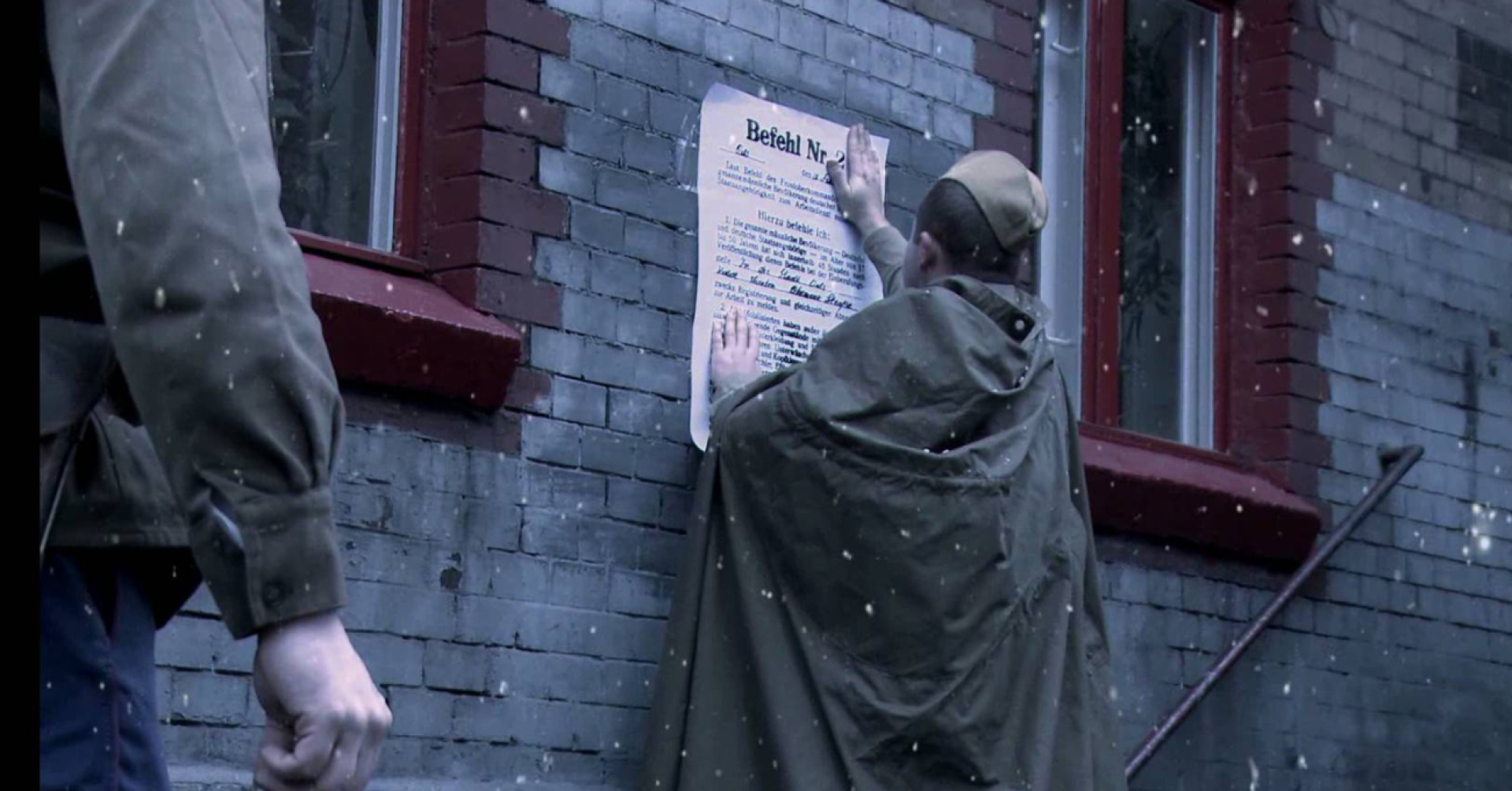 Kadr z filmu, młody chłopak zawiesza ogłoszenie o deportacji na ścianie budynku.