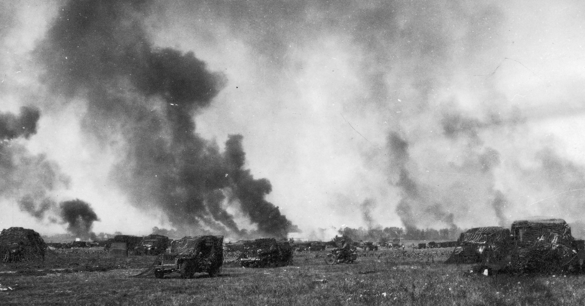 ! Dywizja Pancerna podczas walk w Belgii, 1944 rok.  Na zdjęciu samochody pancerne i unoszący się nad polem bitwy dym.