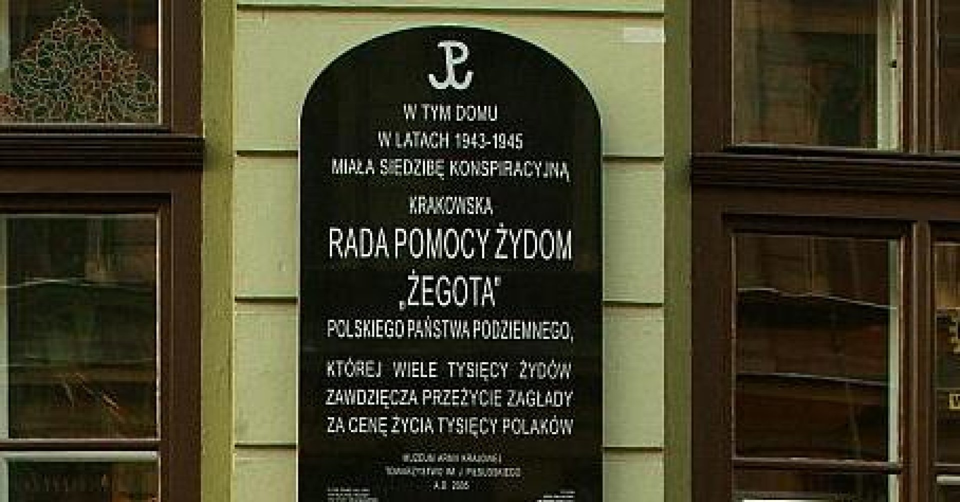 Tablica umieszczona na ścianie kamienicy między dwoma oknami