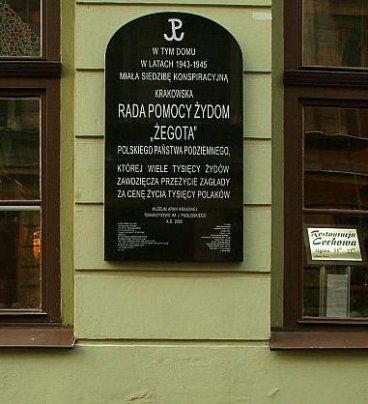 Tablica umieszczona na ścianie kamienicy między dwoma oknami