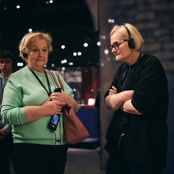 Przestrzeń wystawy czasowej. Kilka dorosłych osób z audioprzewodnikami wsłuchuje się w treść nagrania. Każda z nich patrzy w inną stronę.