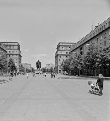 Widok na pomnik Lenina na końcu szerokiej alei, na pierwszym planie kobieta z dzieckiem w wózku, w głębi sylwetki spacerowiczów.