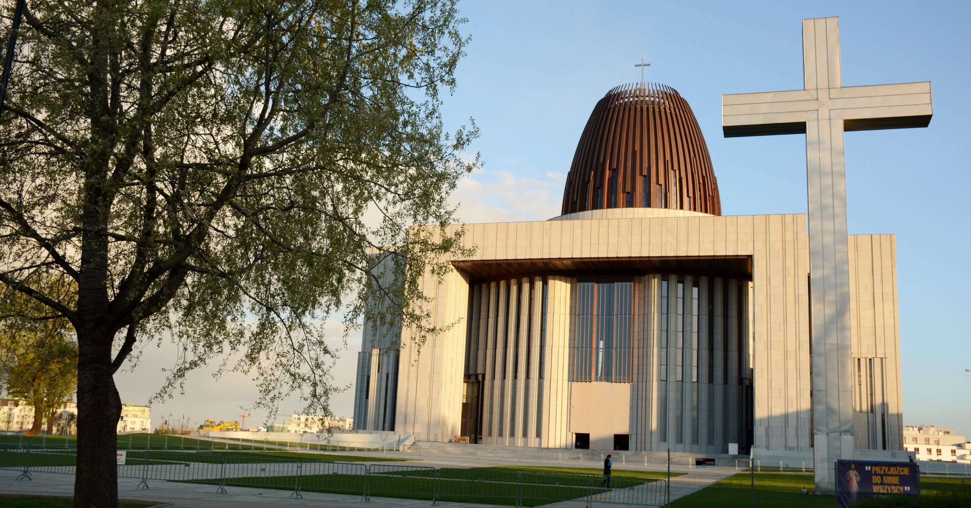 Nowoczesna bryła świątyni, po lewej wysoka brzoza, po prawej duży krzyż.