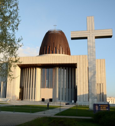 Nowoczesna wielka bryła świątyni, po lewej wysoka brzoza, po prawej duży krzyż.