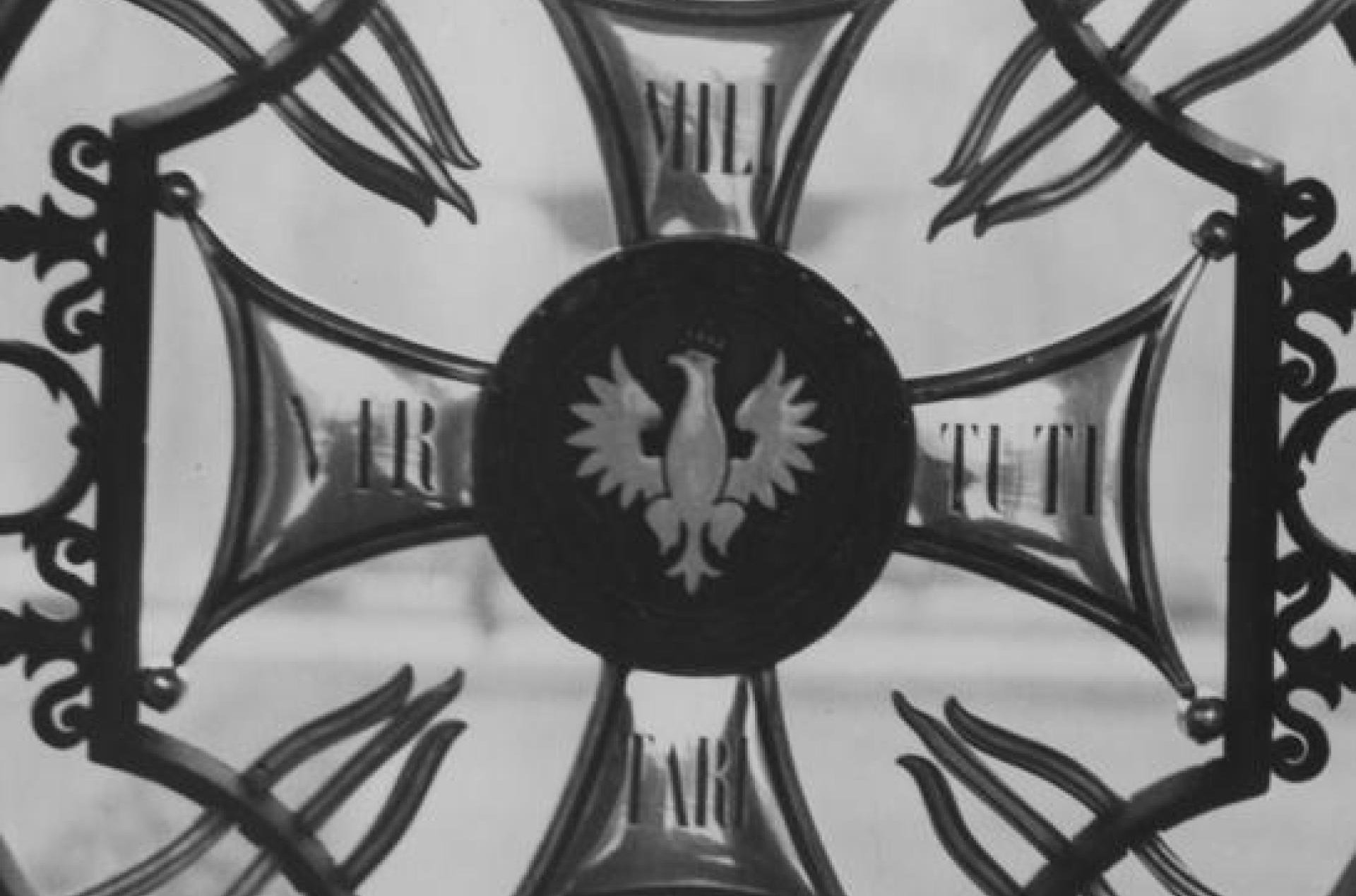 Metalowe okratowanie żelazne z krzyżem z orłem w środku otoczonym powyginanym ormanentem