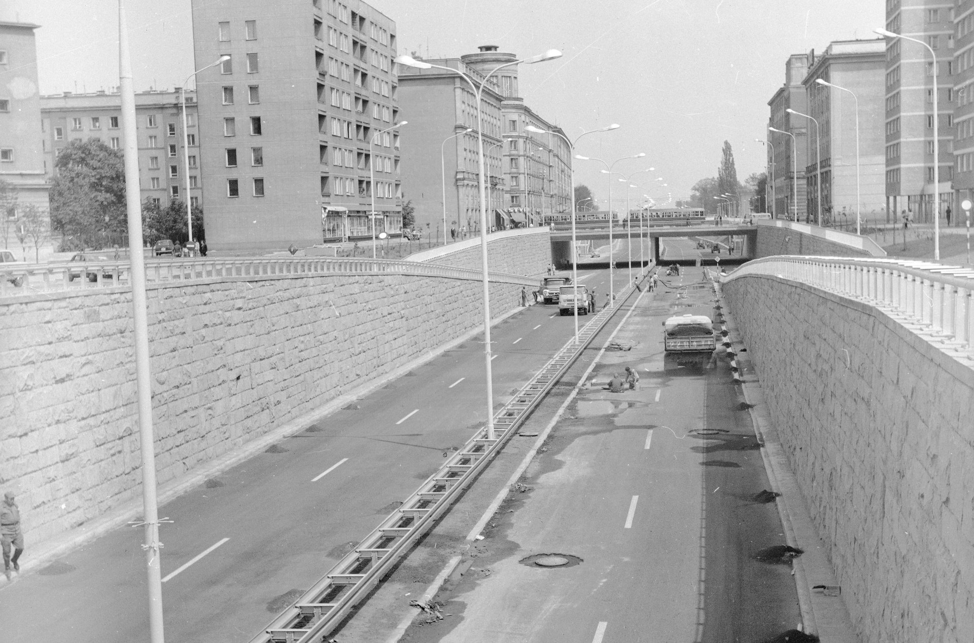 Widok na wyjazd z tunelu z drogą szybkiego ruchu, po której jadą nieliczne samochody. Po obu stronach trasy wysokie bloki mieszkalne. Zdjęcie czarno-białe.