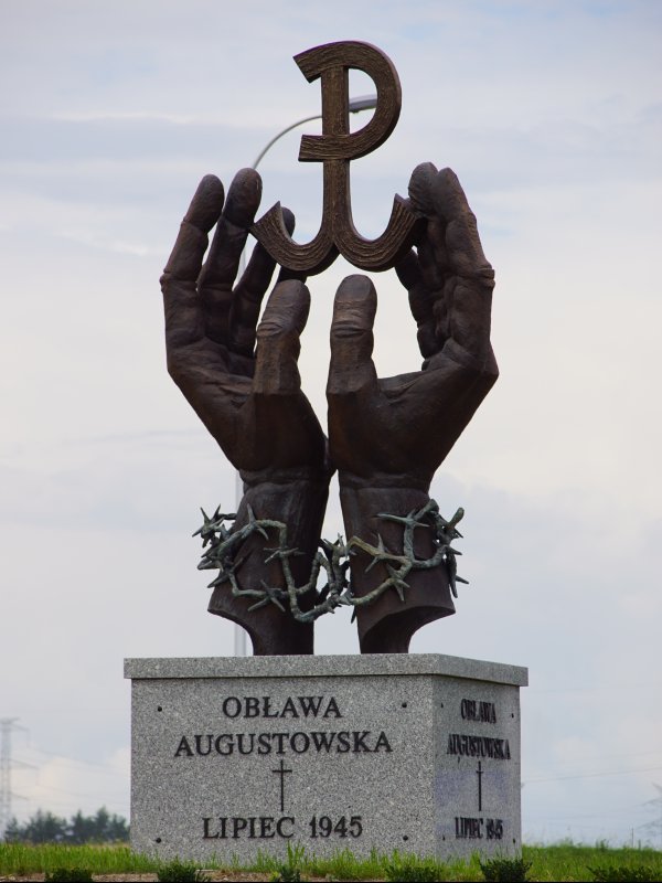 Zdjęcie przedstawia pomnik w kształcie dwóch dłoni spętanych drutem kolczastym. Dłonie trzymają kotwicę - znak Polski Walczącej.