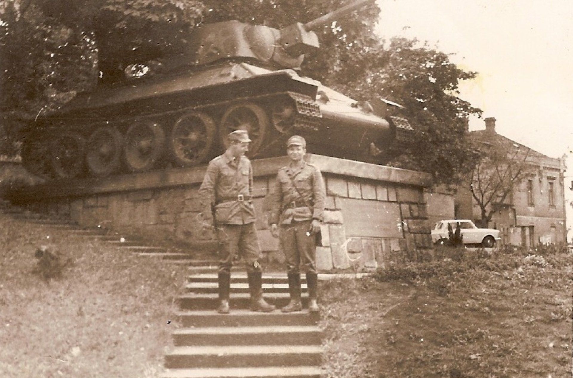 Dwóch żołnierzy stoi na schodkach przed czołgiem na postumencie - spłowiała fotografia czarno-biała