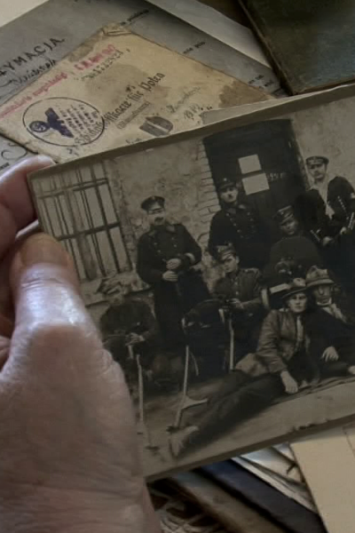 Stary dokument i czarnobiałe zdjęcie w dłoniach. W tle na blacie wiele dokumentów i starych fotografii.