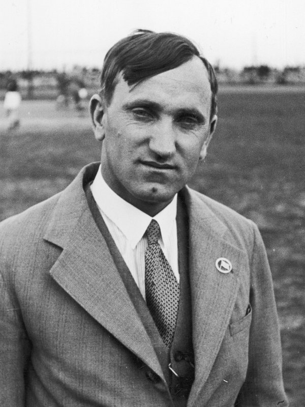 Zdjęcie przedstawia Józefa Kałużę - mężczyznę w średnim wieku, z pociągłą twarzą, długim nosem, dołeczkiem w brodzie. Sportowiec ma na sobie garnitur i krawat. 