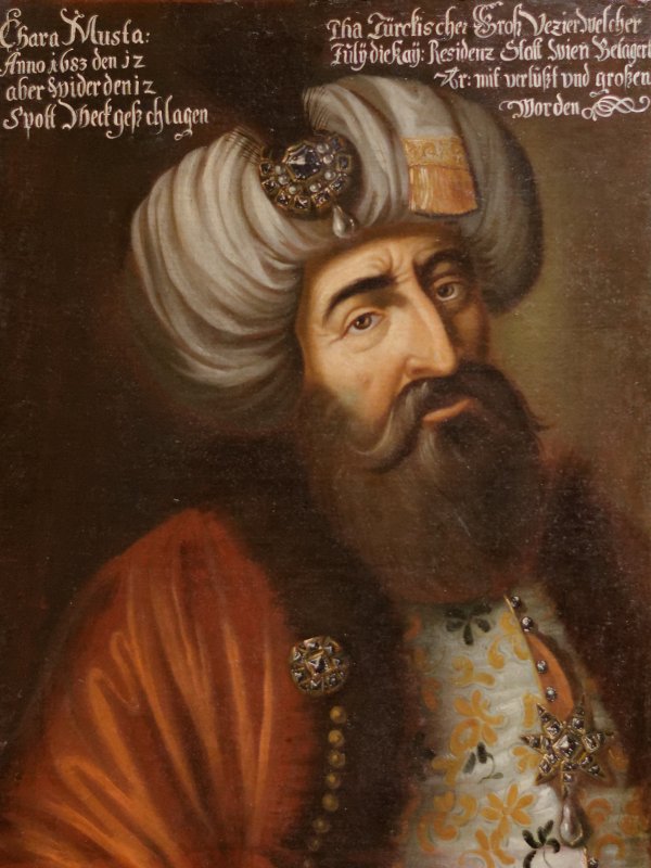Zdjęcie przedstawia portret Kara Mustafy. Mężczyzna ma duży, orli nos,  obfitą, ciemną brodę, długie wąsy i gęste, czarne brwi.  Na głowie nosi biały turban.