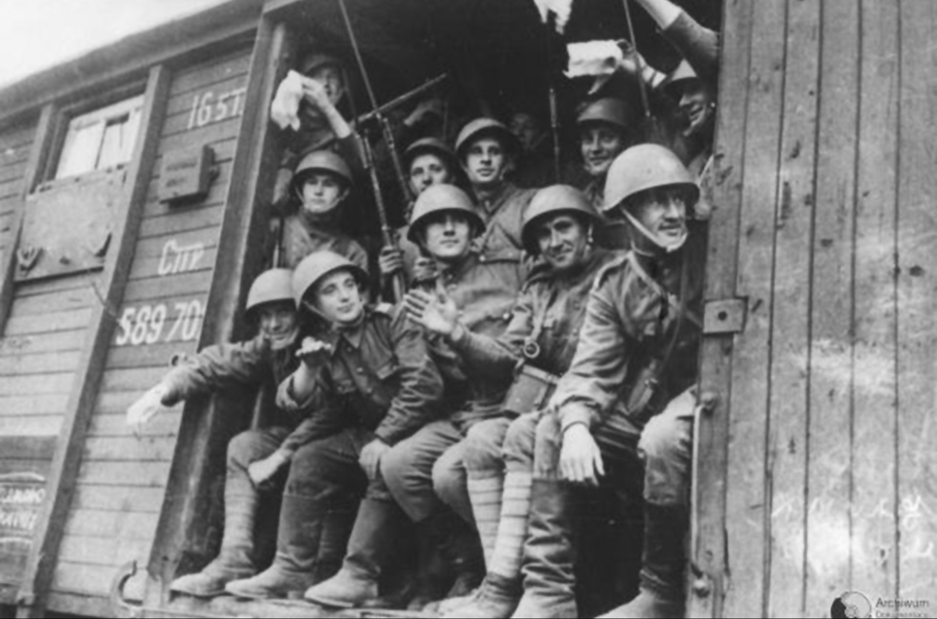 Żołnierze w hełmach wyglądający z otwartych drzwi wagonu w pociągu jadącym na front