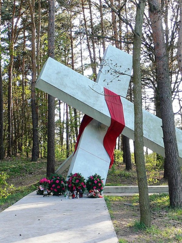 Las. Pomnik w kształcie przewróconego krzyża przepasanego czerwoną szarfą.