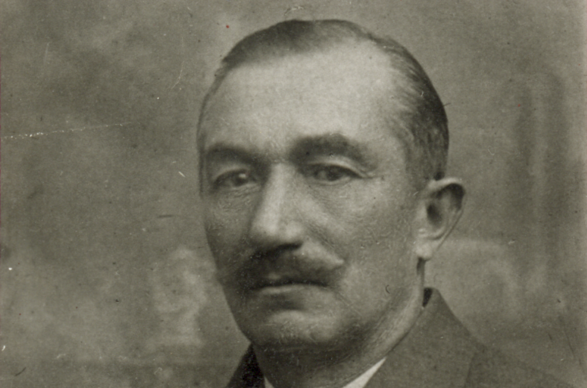 Mężczyzna w podkręconym wąsem; zdjęcie portretowe w jasnym garniturze z kamizelką.