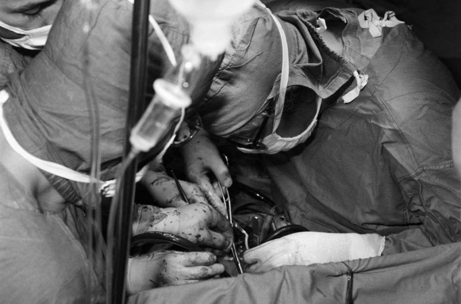 Czarno-białe zdjęcie operacji - lekarze z narzędziami chirurgicznymi pochylają się nad pacjentem.