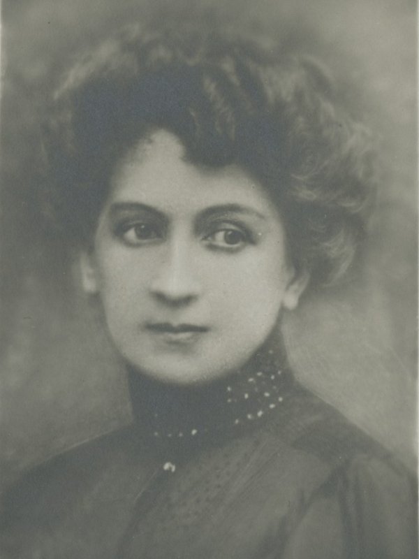 Fotografia przedstawia piękną, młodą kobietę o dużych oczach i zamyślonym spojrzeniu. Gęste, kręcone włosy ma upięte w kok. 