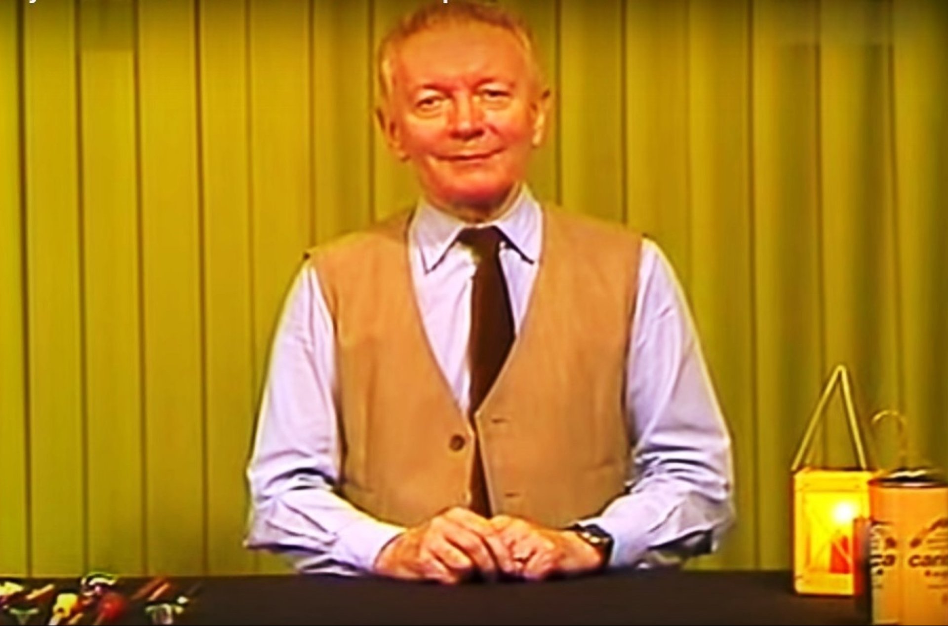 Jasnowłosy mężczyzna w białej koszuli z ciemnym krawatem i żółtej marynarce siedzi na tle żółtej ściany.