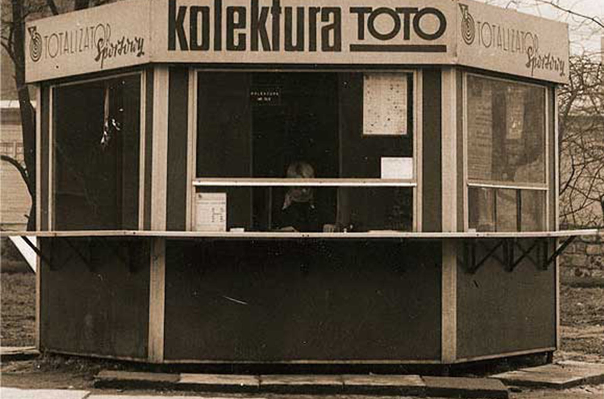 Zdjęcie w kolorze sepii przedstawiające kiosk z napisami: Totalizator Sportowy, Kolektura TOTO