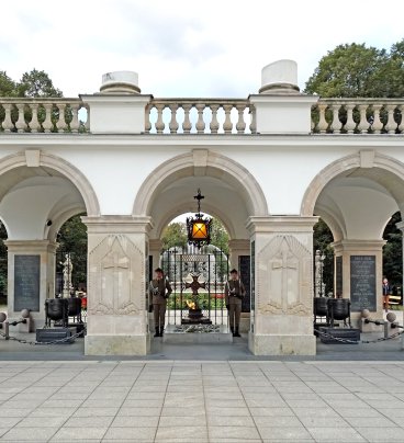 Grób Nieznanego Żołnierza. Widoczna warta honorowa i płonący znicz. W tle - zielone drzewa Ogrodu Saskiego. 