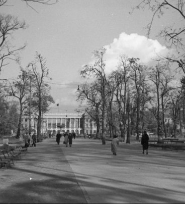 Szeroka aleja parkowa ze spacerującymi ludźmi. W dali widoczne arkady Pałacu Saskiego.