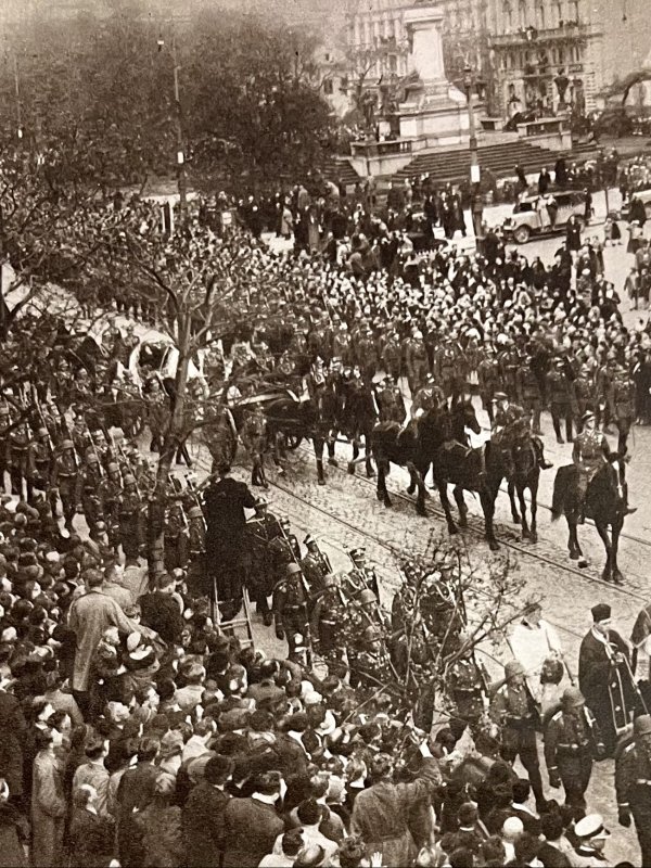 Zdjęcie przedstawia kondukt pogrzebowy na warszawskiej ulicy. Na czele konduktu jadą ułani na koniach. Dalej maszerują żołnierze. Na chodnikach stoją tłumy ludzi.