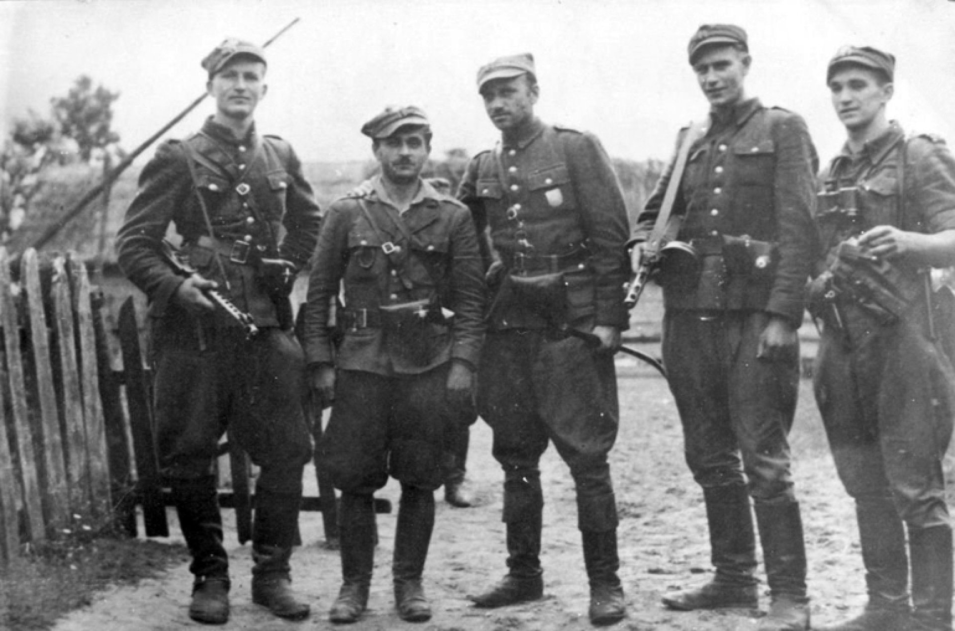 Zdjęcie grupowe pięciu żołnierzy stojących przy płocie.
