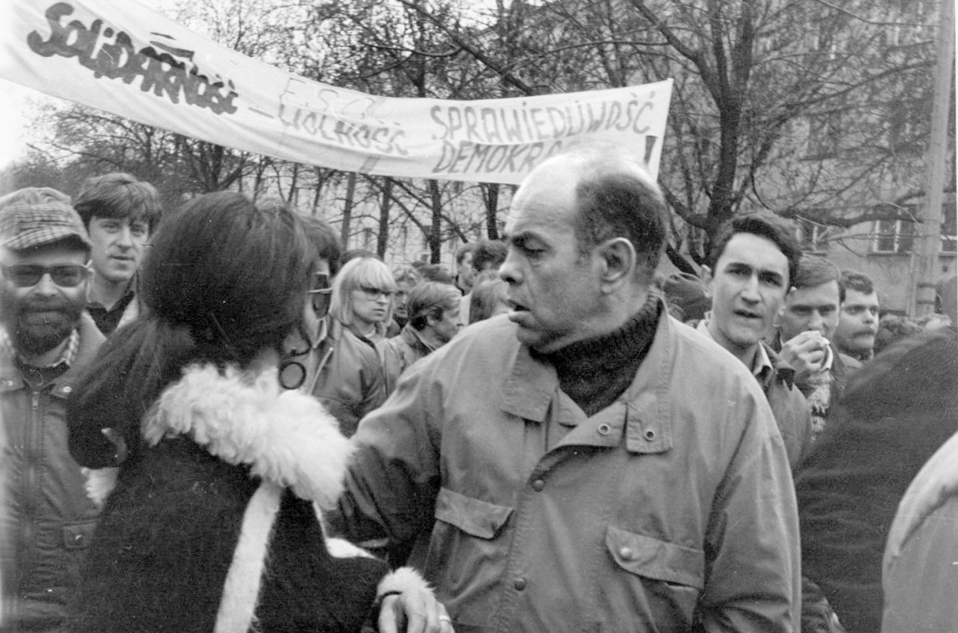 Demonstracja z transparentem Solidarności. Na pierwszym planie łysiejący mężczyzna w jasnej kurtce