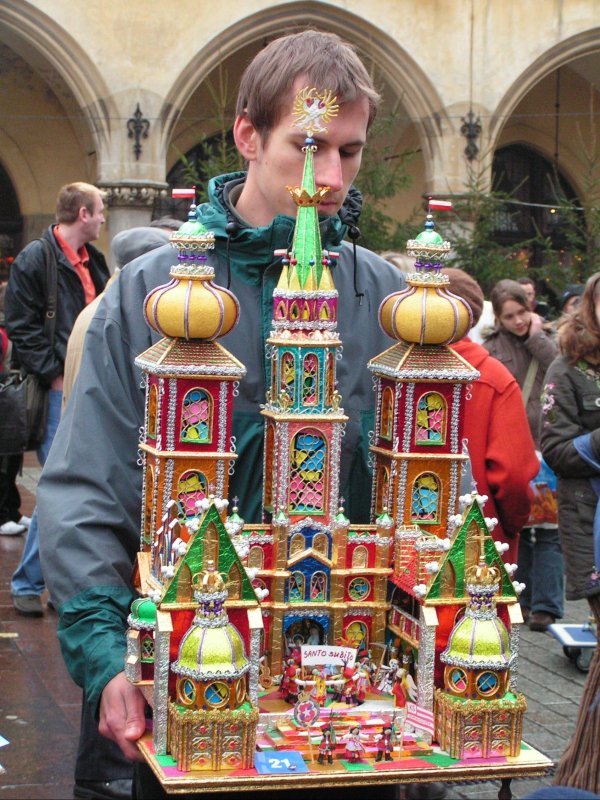 Młody mężczyzna trzyma w rękach kolorową szopkę krakowską.