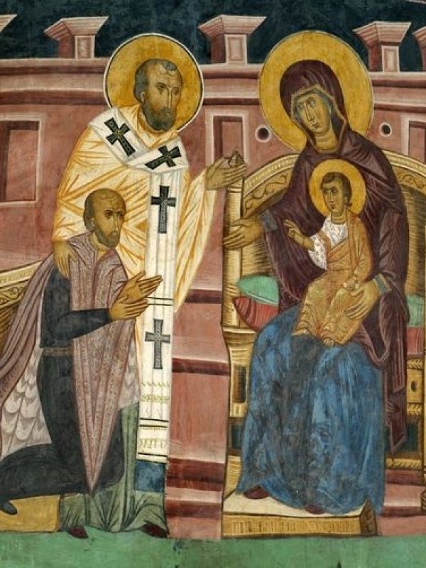 Król klęczy przed tronem, na którym siedzi Maryja z Dzieciątkiem Jezus na kolanach. Jezus błogosławi Jagiełłę. Przy królu stoi święty, który położył rękę na jego ramieniu. W tle mury jakiegoś miasta.   