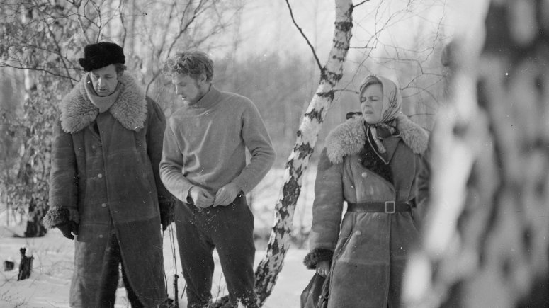 W zaśnieżonym lesie stoją: Andrzej Wajda w długim kożuchu i futrzanej czapce, Daniel Olbrychski w ciemnych spodniach i jasnym golfie, młoda kobieta w kożuchu i chustce na głowie. 