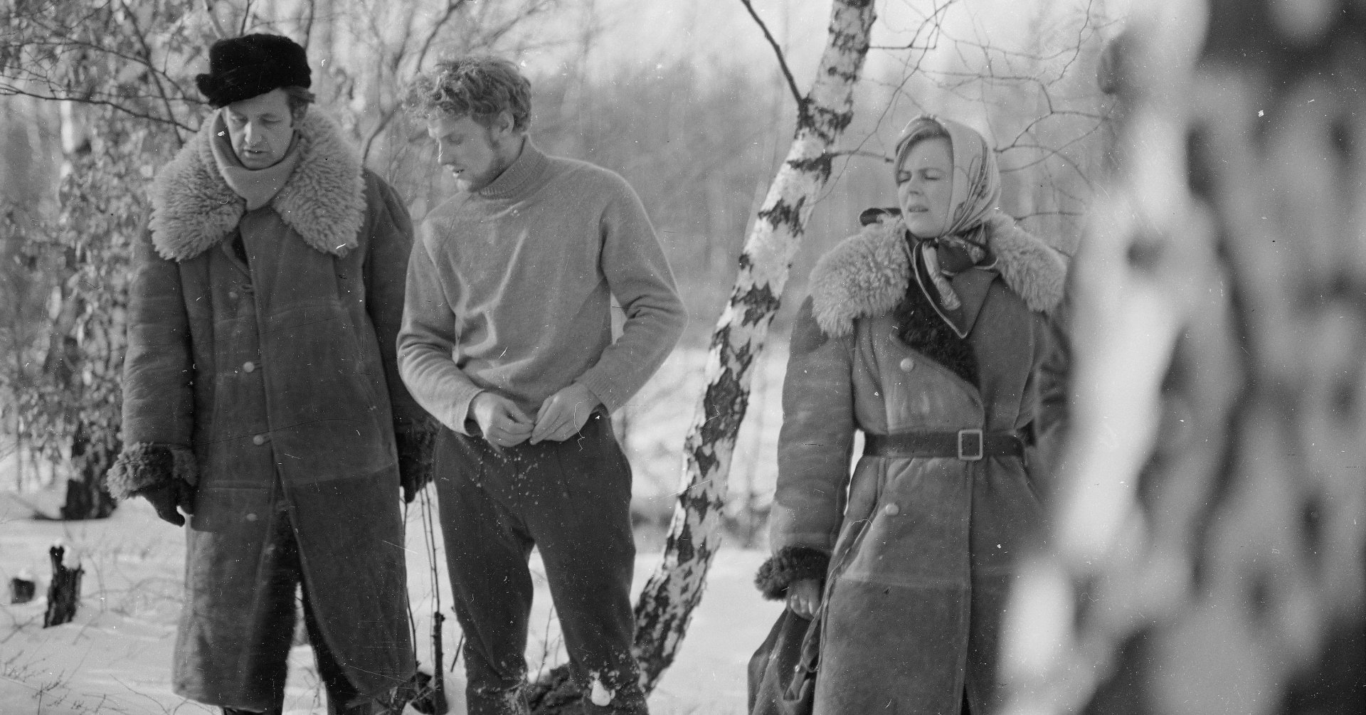W zaśnieżonym lesie stoją: Andrzej Wajda w długim kożuchu i futrzanej czapce, Daniel Olbrychski w ciemnych spodniach i jasnym golfie, młoda kobieta w kożuchu i chustce na głowie. 