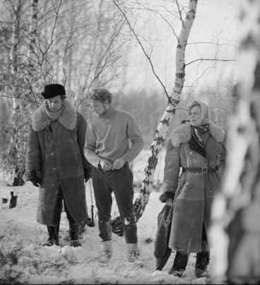 W zaśnieżonym lesie stoją: Andrzej Wajda w długim kożuchu i futrzanej czapce, Daniel Olbrychski w ciemnych spodniach i jasnym golfie, młoda kobieta w kożuchu i chustce na głowie. 