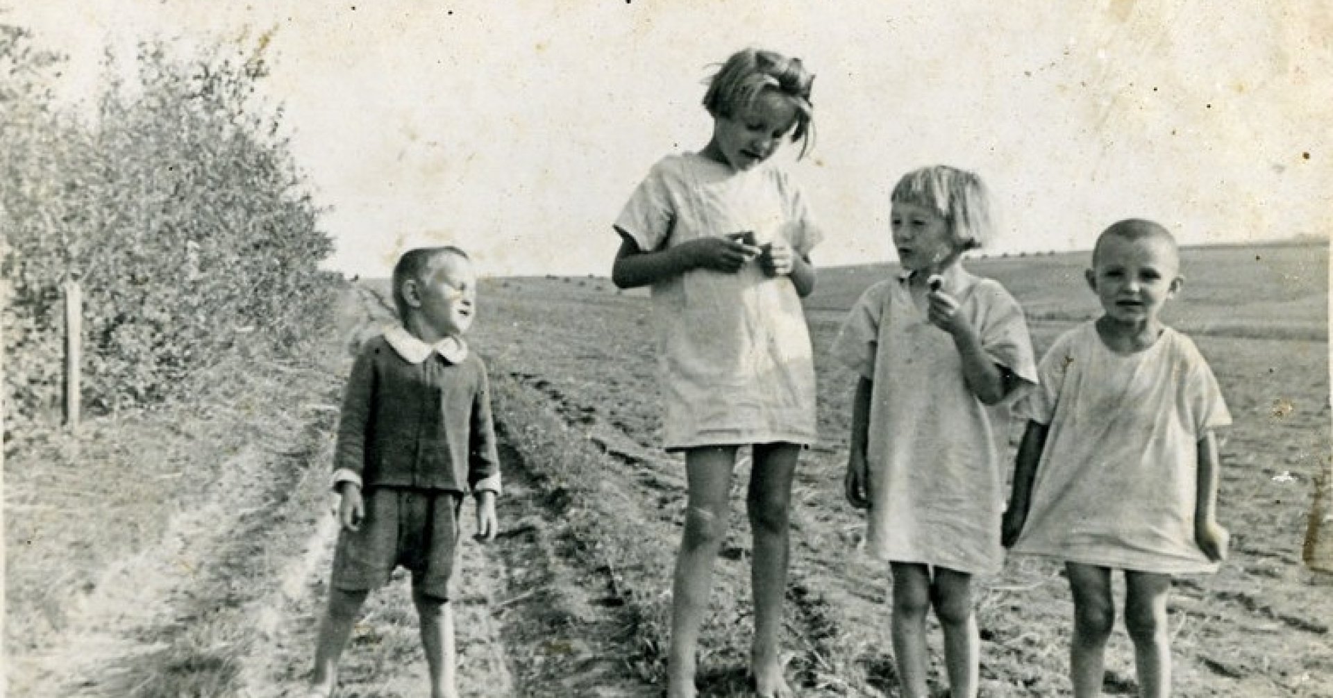 Czworo bosych dzieci w krótkich lnianych ubrankach stoi na polnej drodze.