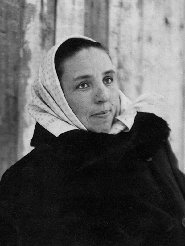 Młoda kobieta w kożuchu i w jasnej chustce na głowie. Ma pogodną, uśmiechniętą twarz.