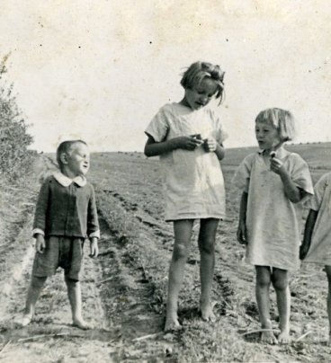 Czworo bosych dzieci w krótkich lnianych ubrankach stoi na polnej drodze.