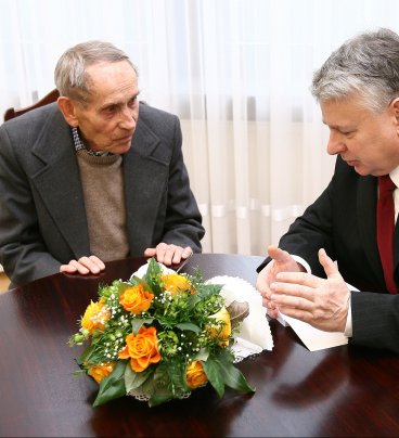 Przy stoliku z bukietem kwiatów siedzą od lewej Konwicki i Borusewicz. Rozmawiają, Borusewicz gestykuluje.