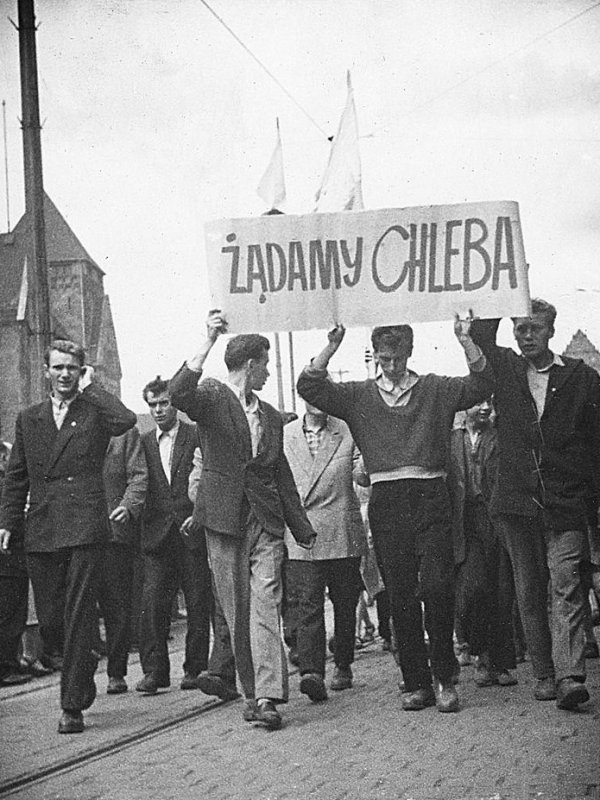 Grupa młodych ludzi niesie transparent z napisem „Żądamy chleba”. Za nimi podąża pochód protestujących.