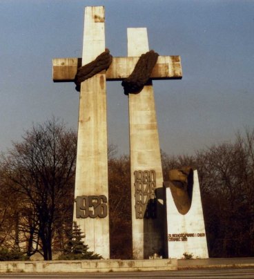 Dwa wysokie krzyże połaczone ze sobą ramionami. Raamiona przewiązane grubym sznurem. Na dole lewego krzyża data: 1956. Na dole prawego krzyża daty: 1968, 1970, 1876, 1980.